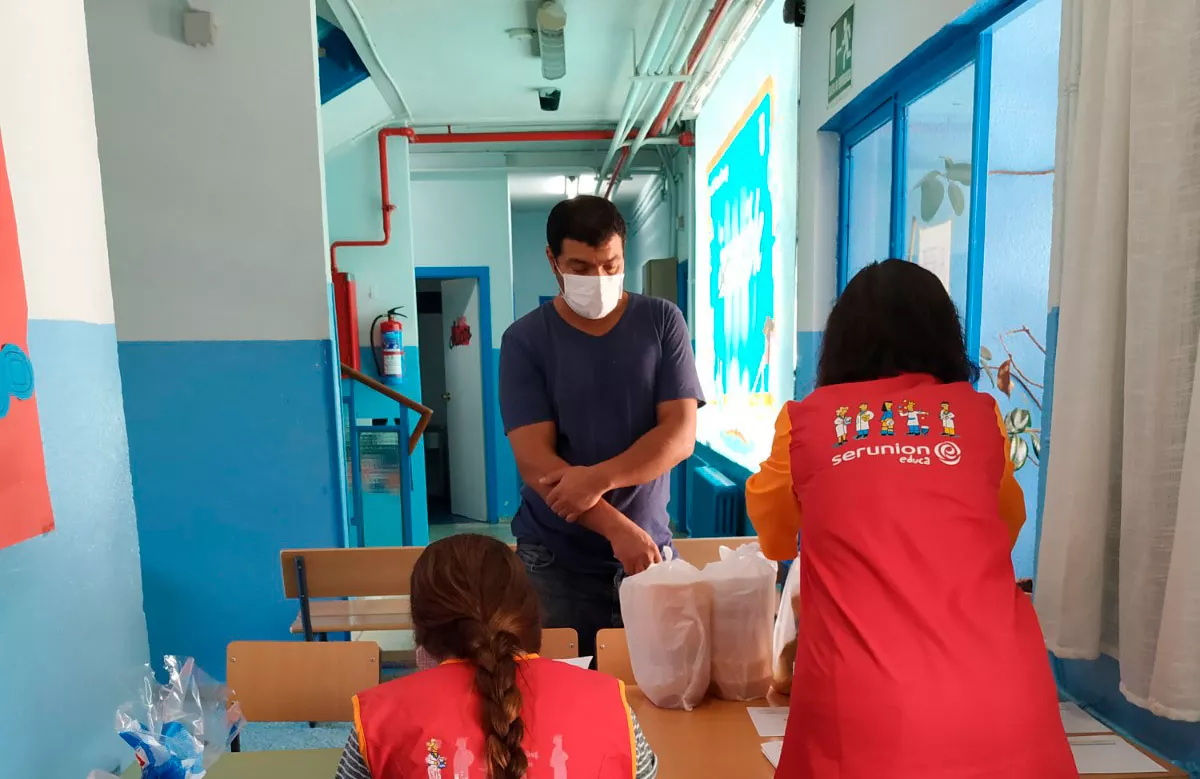 Dos trabajadoras de Serunion entregando los menús a un padre en el colegio Santo Domingo de Vallecas.